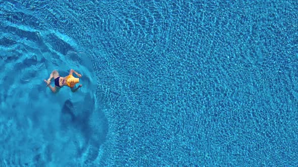 View From the Top As a Woman in a Blue Swimsuit and a Big Yellow Hat Swims in the Pool