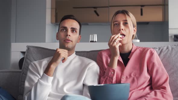 Happy Young Couple Watching Funny Show on TVeating Popcorn at Home Lying on Sofa Together. People