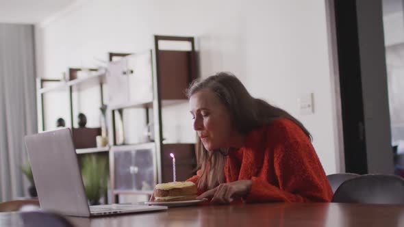 Woman blowing candle on the cake while having a video chat on her laptop at home