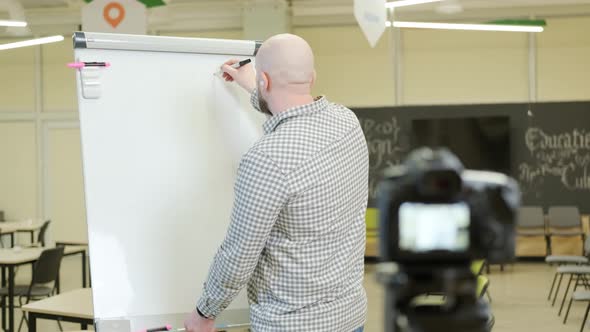 Teacher Records Video Lessons He Stands and Writes with a Pen on a Flip Chart