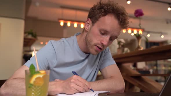 Handsome man sitting in a cafe writes something in his notebook.