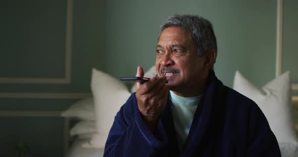 Smiling senior mixed race man sitting on bed using smartphone