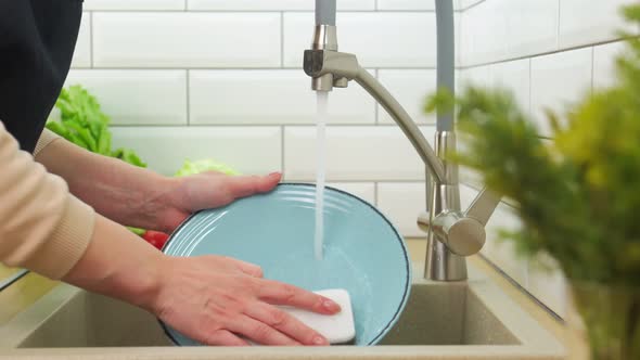 Woman Hands Rinse Plate at the Kitchen Sink  Doing the Chores at Home