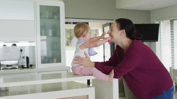 Caucasian mother kissing while playing with her baby in the kitchen at home