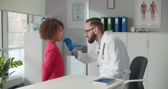 Male Doctor Giving African Little Girl Checkup in Clinic Office