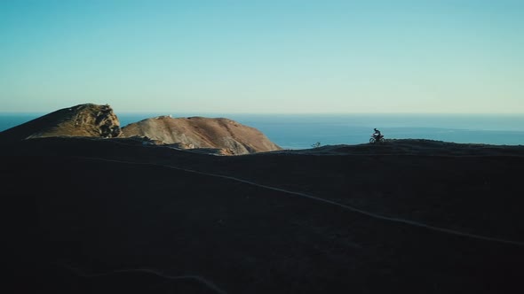 Drone View of Man on Motorbike Extremely Rides Across the Hills with Black Sea on Background in