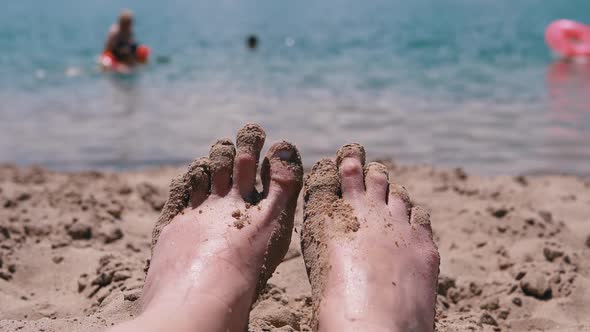 POV Female Wet Feet in Sand Lying on a Sandy Beach in Sun Glare Near the Sea
