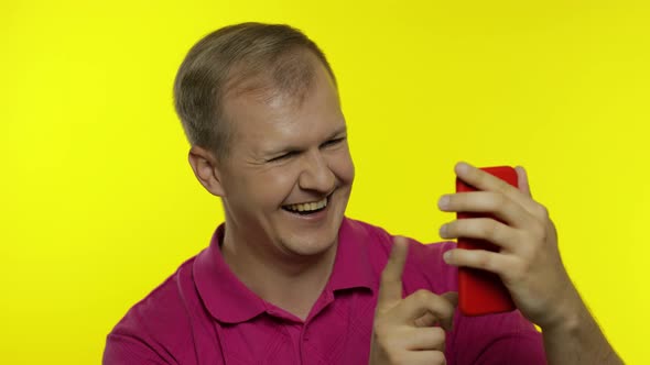 Young Man Posing in Pink T-shirt. Handsome Guy Using Mobile Phone, Watching Funny Videos Online