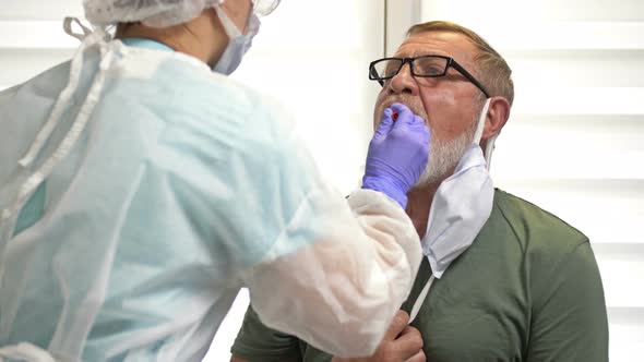 Lab Technician in a Protective Suit Takes a Swab From an Elderly Patient for Coronavirus.