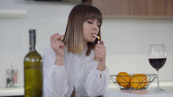 Medium Shot Portrait of Slim Beautiful Young Woman Lighting Cigarette Smoking in Kitchen at Home