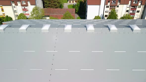 Flying beside big building roof covered with insulation panels and white polyester light domes. Aeri