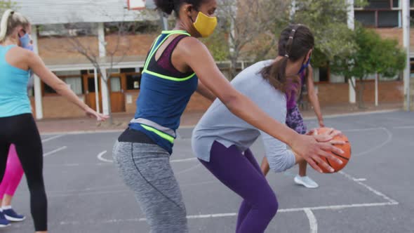 Diverse female basketball team wearing face masks playing match, scoring goal