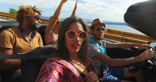 Attractive young people enjoying music while driving in convertible