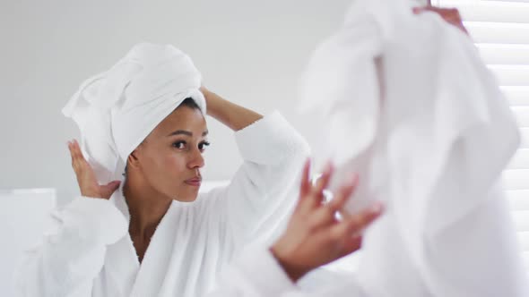 African american woman in bathrobe touching her head looking in the mirror at bathroom
