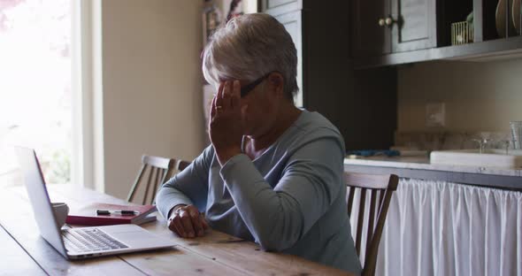 Senior mixed race woman using laptop in kitchen removing glasses