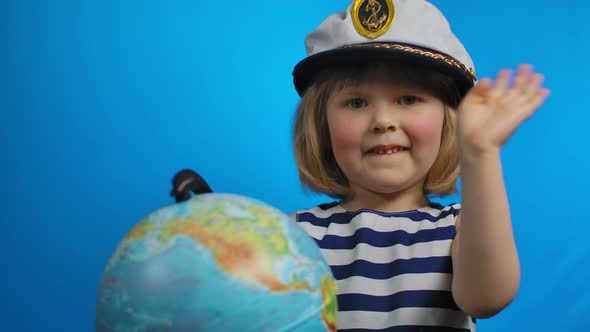 Little Baby Girl in Sailor Hat is Holding the Globe and Waving Her Hand