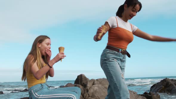 Side view of a Caucasian and a mixed race girl eating ice cream seaside