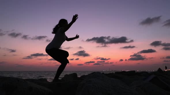 Silhouette shot of a woman practicing Yoga standing position with her legs and arms crossed, shot du