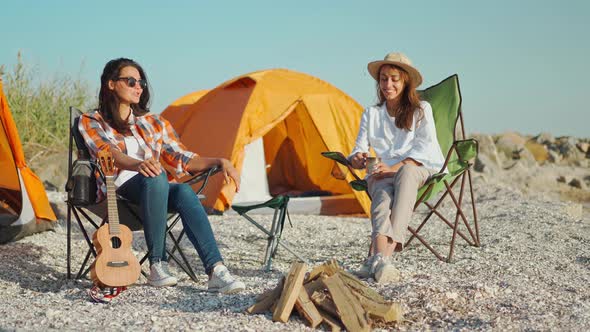 Couple Charming Beautiful Women Girlfriends Sitting in Camping Chairs at Sea Coast Have Fun Talking