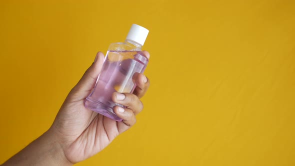 Hand Hold a Mouthwash Liquid Container on Yellow Background