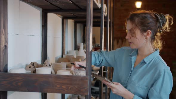 Young Woman Checking Hand-made Pots and Taking Notes in Pottery Studio