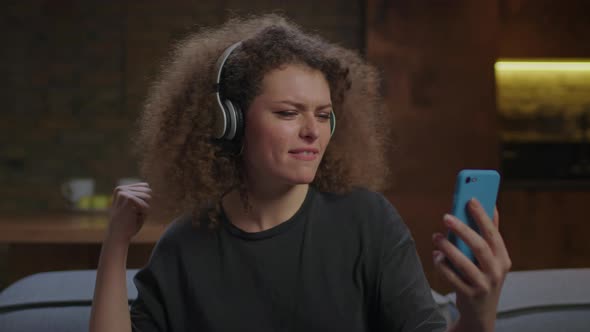 Millennial Woman Singing Songs Looking at Mobile Phone and Wearing Wireless Headphones