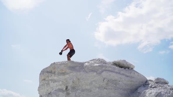 strong man lifting kettlebell on white hill.