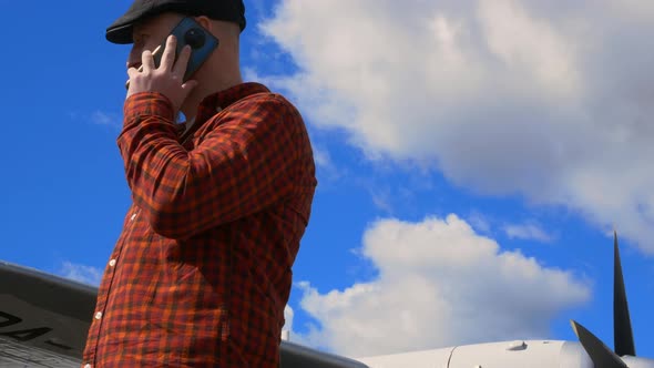 A Bearded White Man in a Headdress Against a Blue Sky Stands Next to an Airplane and Talks on a