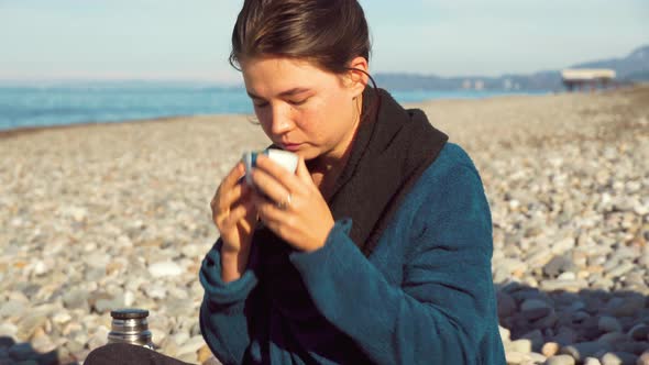 woman holds a teacup and thoughtfully looks deep into herself on the seashore.