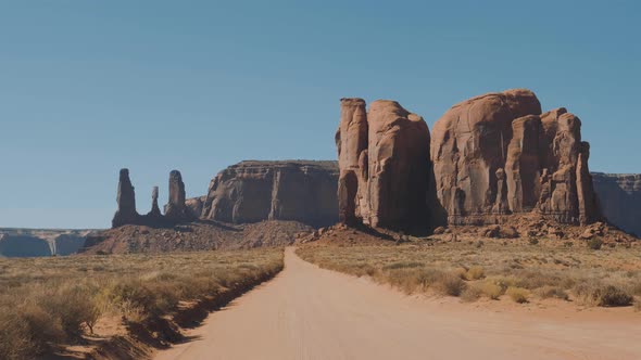 Driving On Dusty Dirt Road In Desert Among Red Rocks Buttes Of Monument Valley