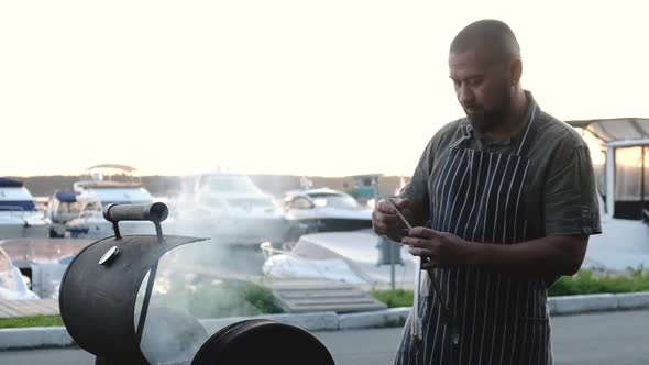 man grilling meat opens metal grill and smears meat with oil with tongs