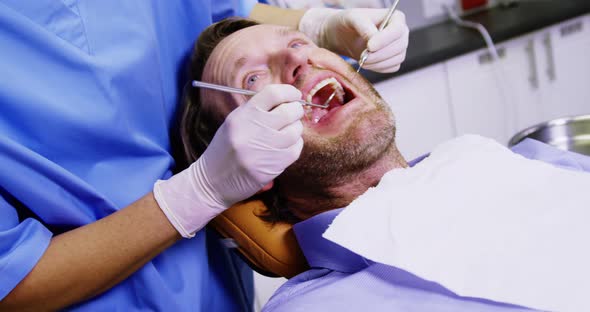 Dentist examining a male patient with dental tools