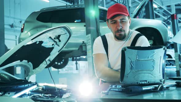 Car Mechanic Using His Laptop to Inspect a Broken Vehicle