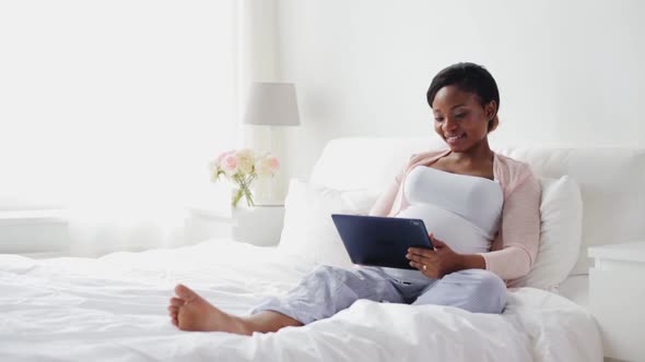 Happy Pregnant Woman with Tablet Pc in Bed 