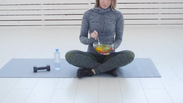 Healthy Food Concept. Happy Woman Eating Healthy Green Salad After Workout in a White Interior