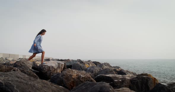 A Young Woman Walks Over Large Boulders Along the Coastline