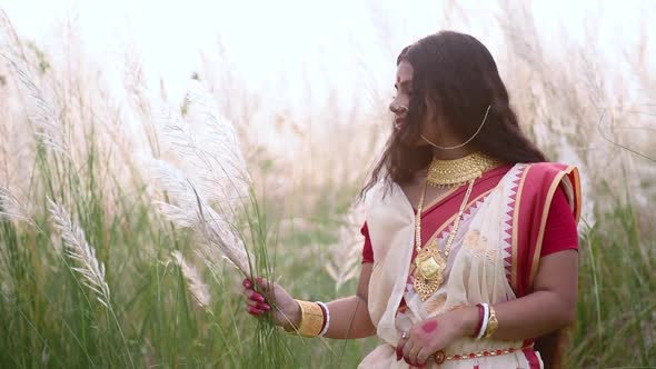 A happy and beautiful Indian bengali woman plays with the long white grass Kaash phool in a field we