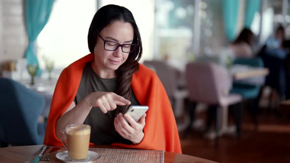 Charming Woman is Viewing Pictures in Social Media and Resting in Coffee Shop Drinking Latte