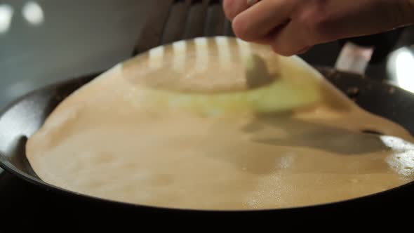 Women's Hands with a Spatula Turn Pancakes in a Frying Pan