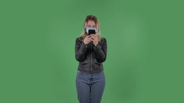 Portrait of Beautiful Young Woman in Medical Mask Is Texting on Her Phone. Blonde with Loose Hair in