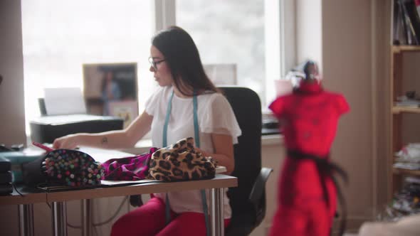 A Woman Designer Sits By the Table  Little Dress Sample on the Foreground