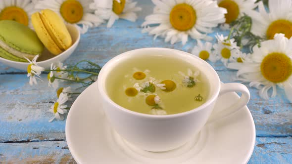 Composition with chamomile flowers, herbal tea and macaroons on vintage light blue wooden tabletop.