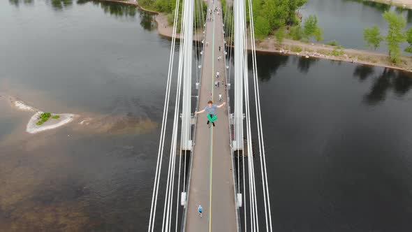 The Man Sits in a Lotus Position on a Rope Stretched Between the Supports of the Bridge at High