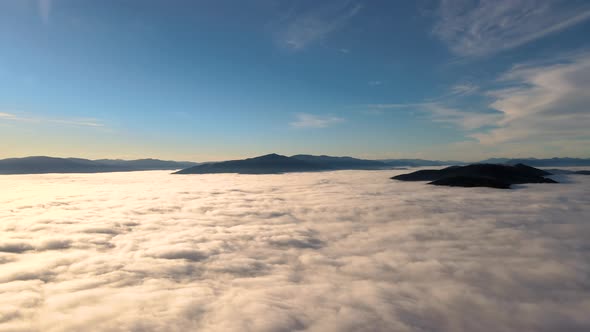 Aerial view of yellow sunset over white puffy clouds with distant mountains on horizon.