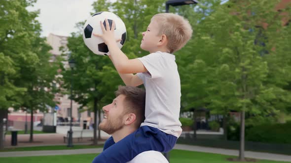 Happy Father Holding Little Son on Shoulders Helping Him to Score Basket on Basketball Playground