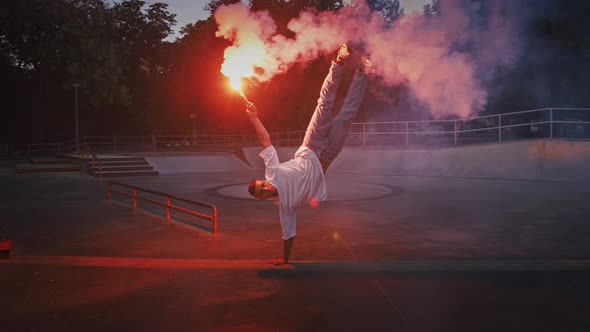 Young Male is Holding Glowing Red Signal Flare and Standing in Stance While Performing Break Dance