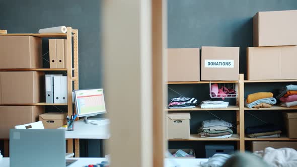 Storage Room with Used Clothes on Shelves and in Cardboard Boxes and Charity Fund Office