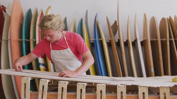 Caucasian male surfboard maker working in his studio and making a wooden surfboard