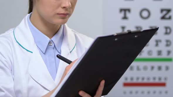 Cheerful Female Ophthalmologist Filling Patient Examination Data, Diagnosis