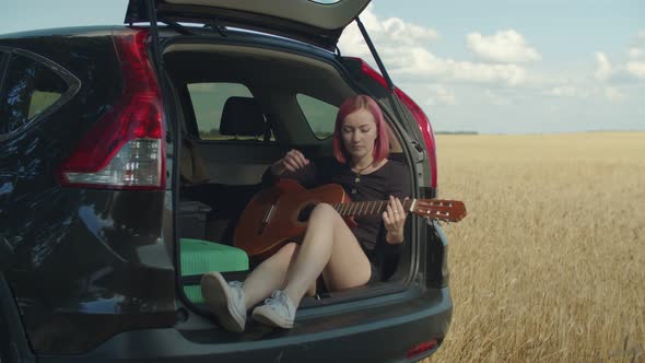 Dreamy Hipster Woman Playing Guitar in Car Trunk